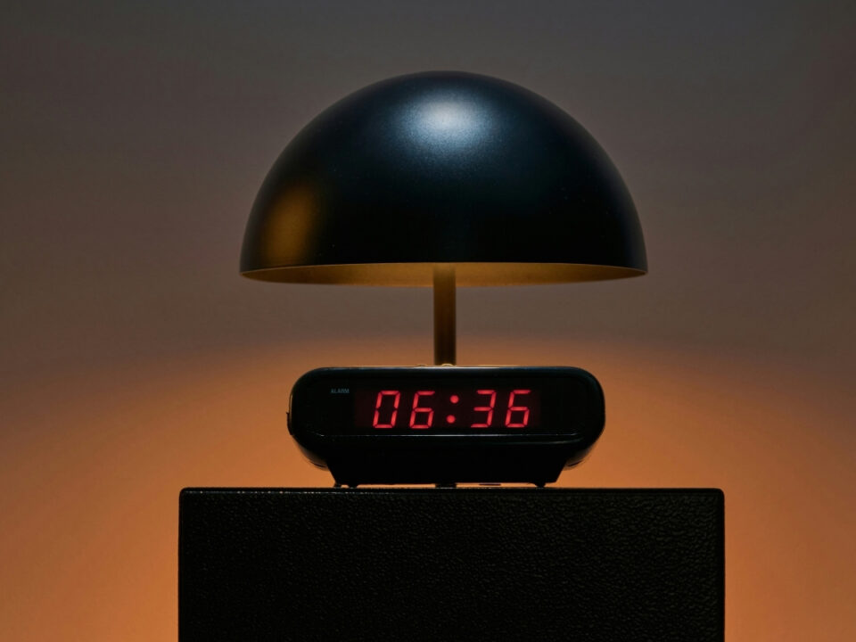 Digitális ébresztőóra 6:36-ot mutat, felette meleg fényű, gomba alakú éjjeli lámpa éjelliszekrényen