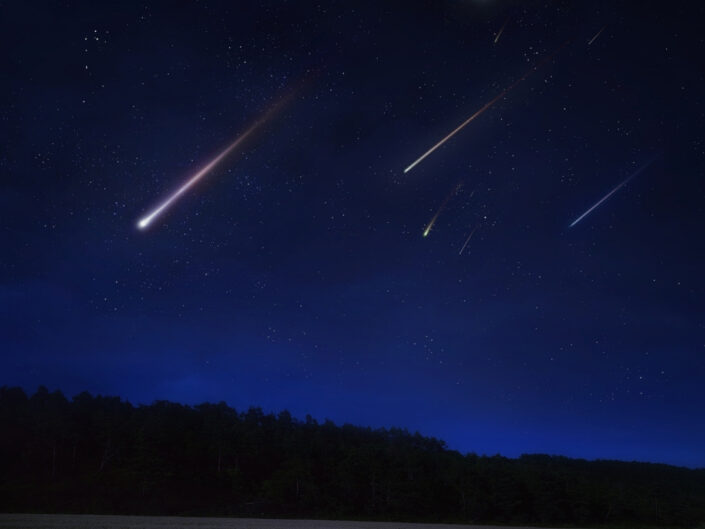 Sötét erdő fölött csillagokkal teli, mélykék égbolt, amelyen több fehér, sárgás és lilás meteor hosszú fénycsíkja látható.