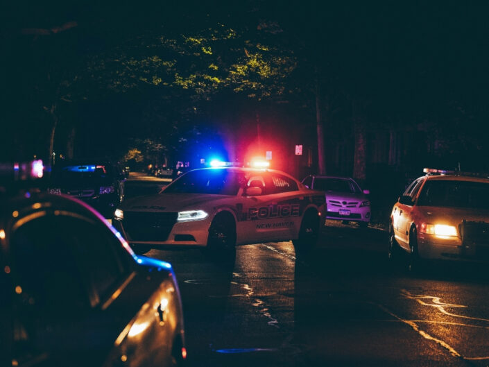 Rendőrautó villogója sötét utcán világít, az autó keresztben áll az úton