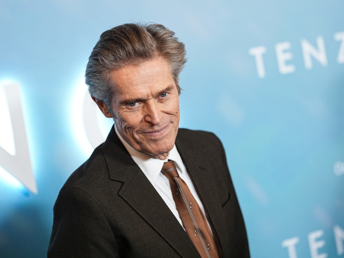 Willem Dafoe premieren mosolyogva néz öltönyben a kamerába